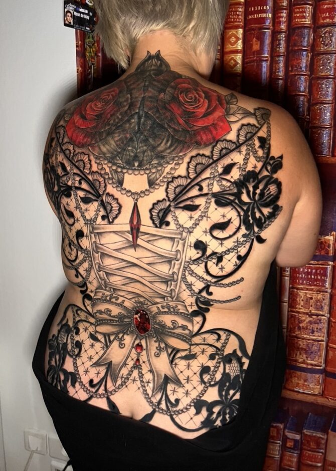 Tattoo-Bijoux avec des roses réalistes rouges et grises pour un cover, un ruban de corset et un noeud avec une pierre à facettes rouges, et de la dentelle noire tout autour pour un dos complet