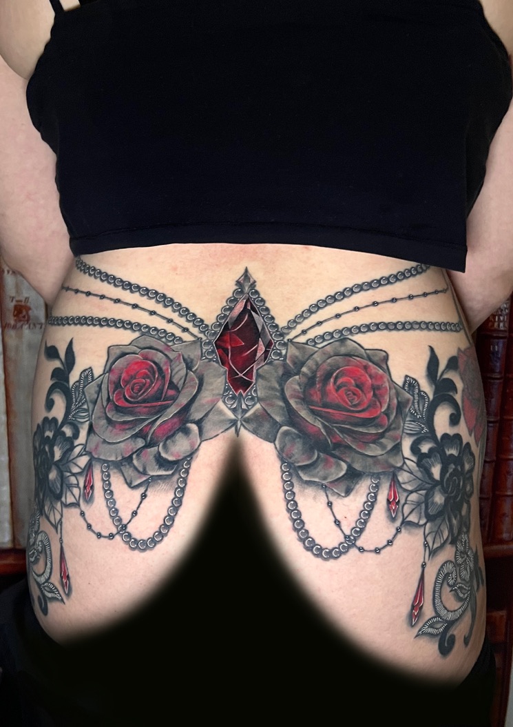 Tattoo-Bijoux en compo reins et fesses, avec une pierre grenat à facettes rouge bordeaux en forme de losange, deux roses réalistes grises et rouges, des fleurs de dentelle
