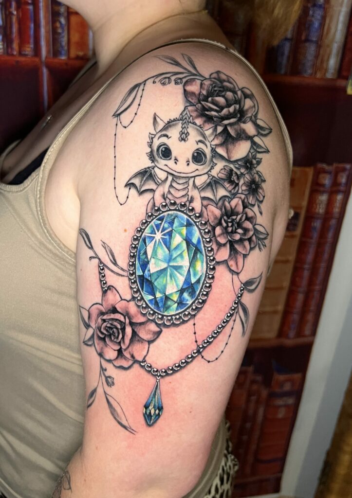 Tattoo-Bijoux avec des fleurs en noir et gris, un petit dragon effet dessin animé pour enfant et une pierre à facettes ovale dans les teintes bleues et vertes